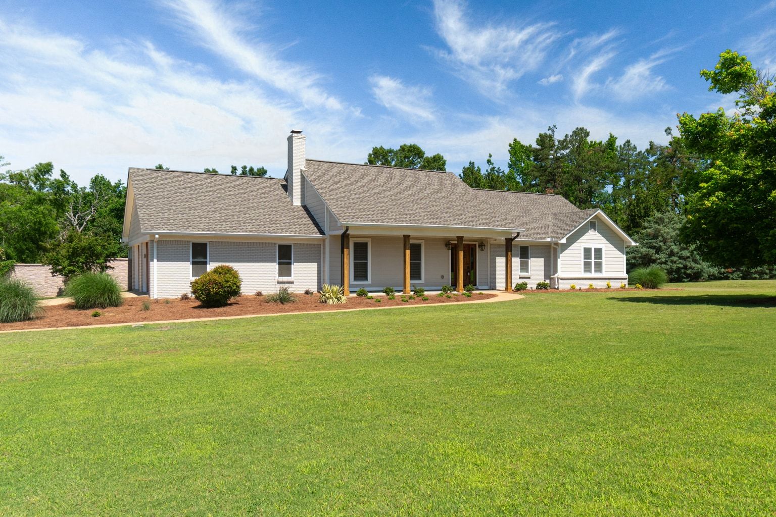 A single-storey white brick ranch with a covered front porch, photographed in flat midday light under a blue sky.